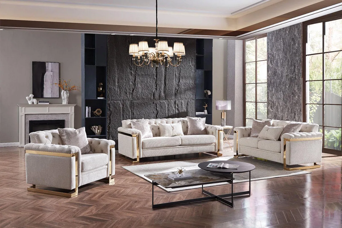 A light-neutral tufted sofa set with structured arms and slim gold-finished trim along the base.